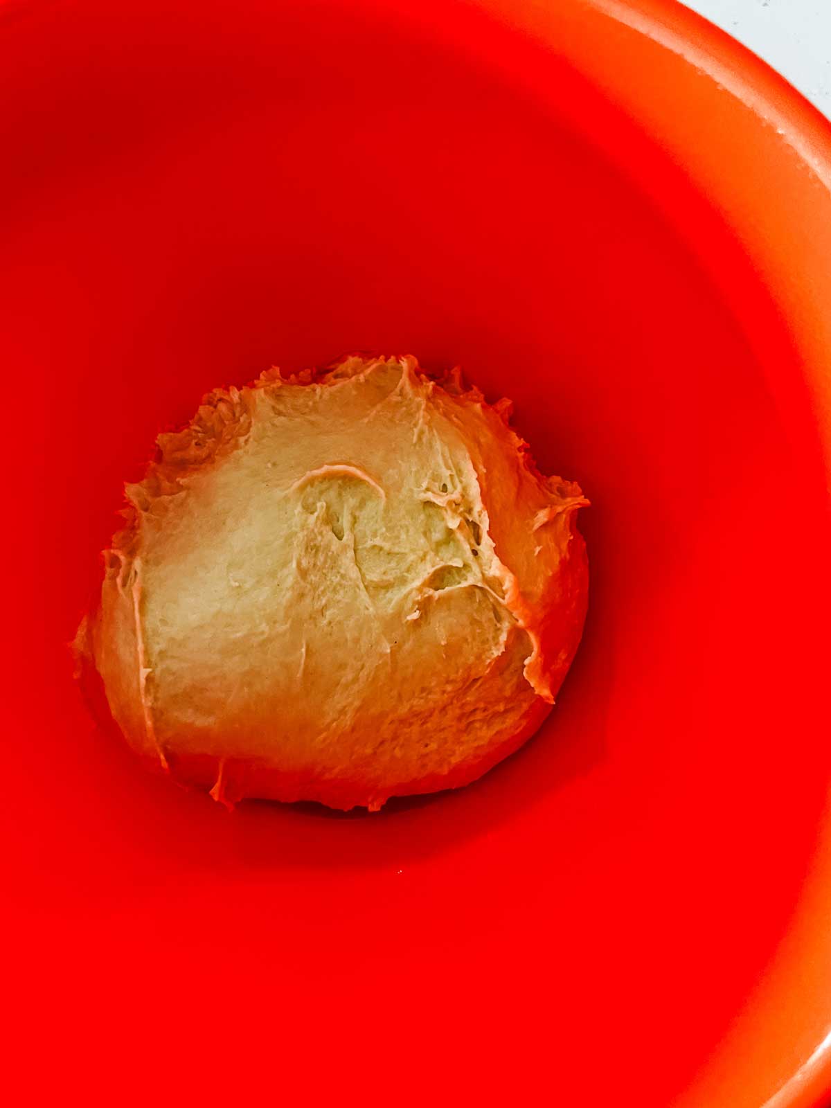 Cinnamon roll dough in an orange bowl ready to rise.