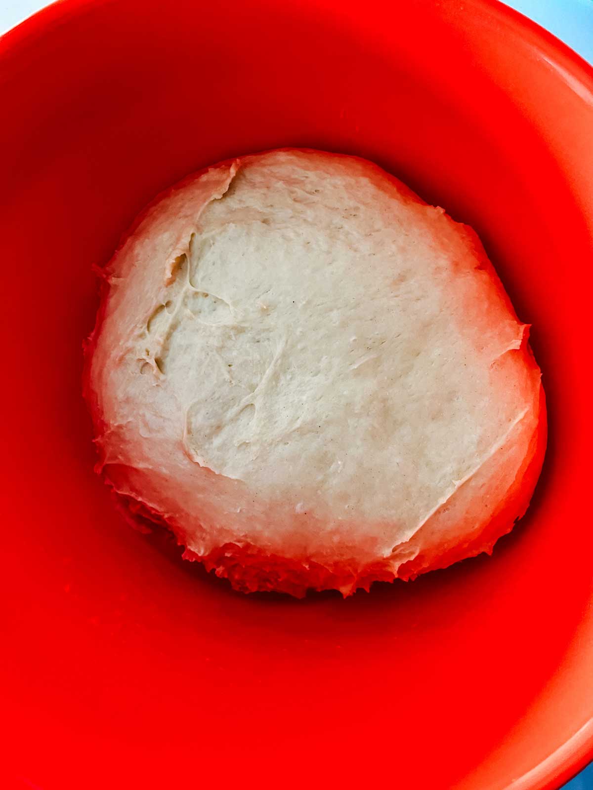 Photo of risen cinnamon roll dough in an orange bowl.