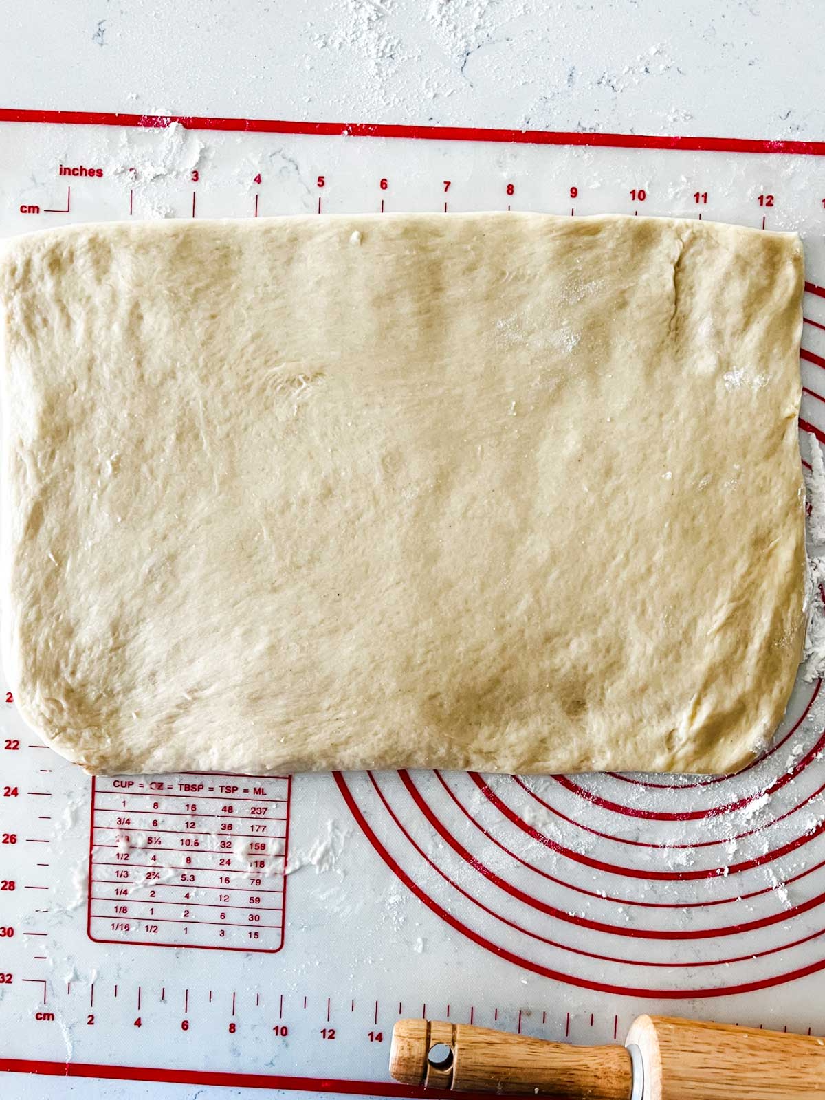 Cinnamon roll dough rolled out on a pastry mat.