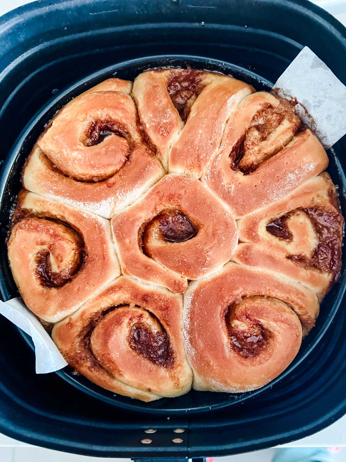 Cinnamon rolls that have just been cooked in a cake pan inside an air fryer basket.
