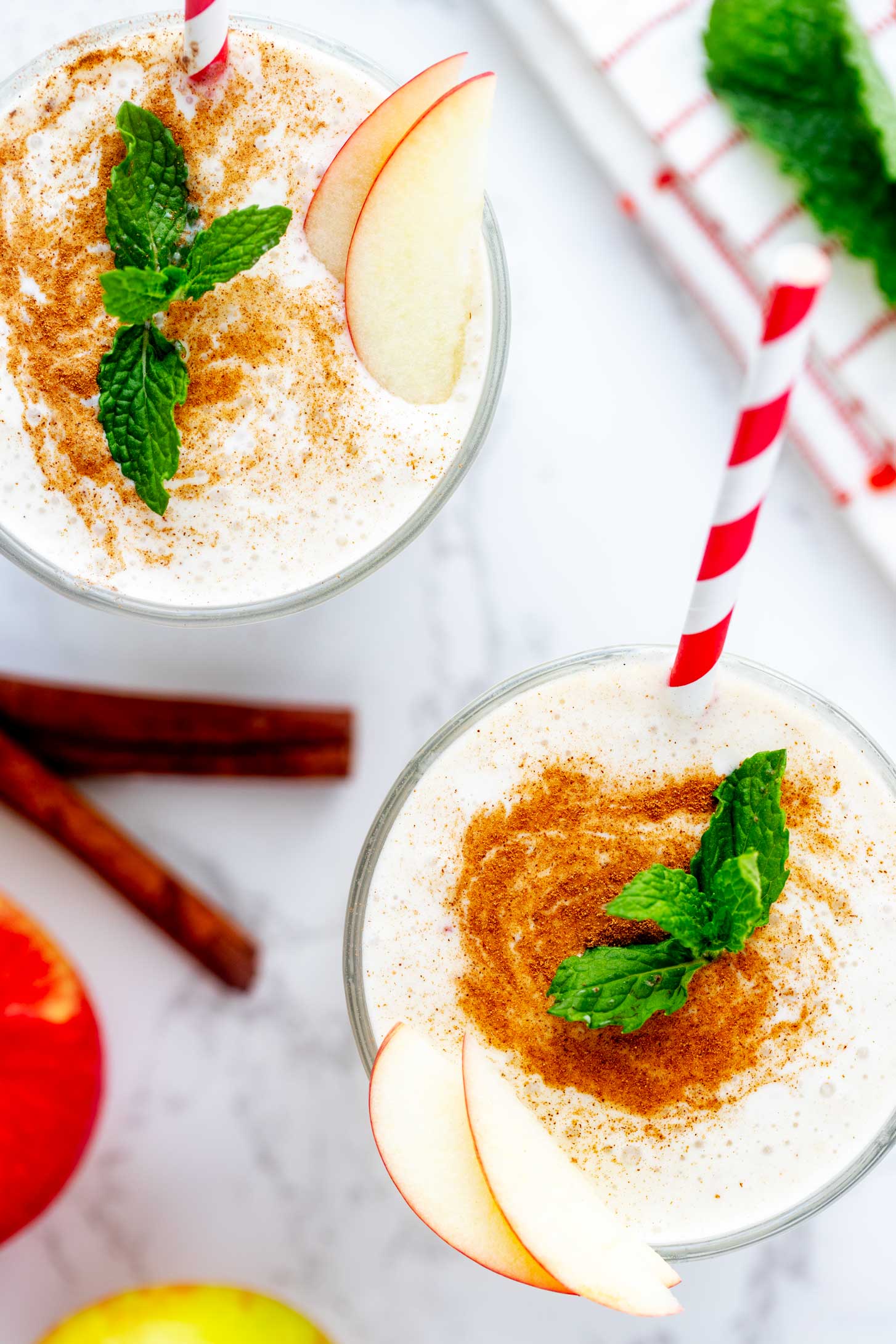 Close up overhead photo of two apple banana smoothies garnished with cinnamon and mint.