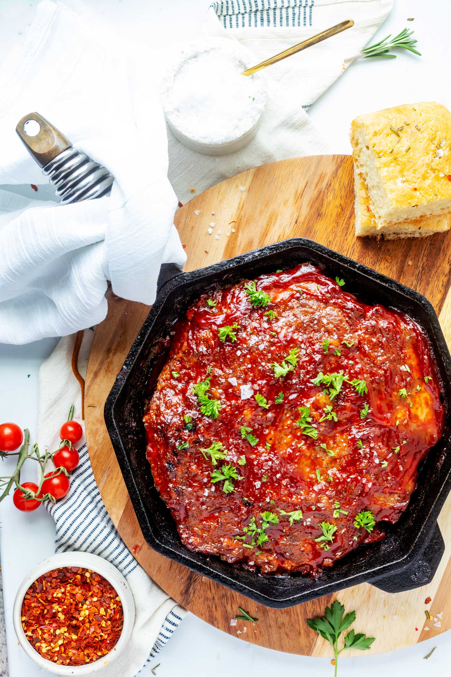 Overhead photo of cast iron meatloaf in a skillet sat on top of a round wooden board.