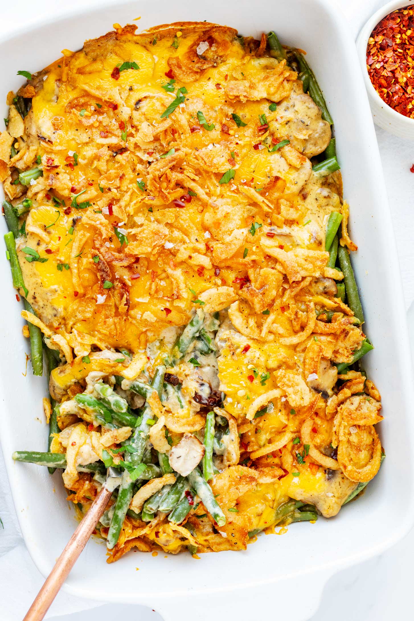 Overhead photo of cheesy green bean casserole in a white casserole dish with a spoon.