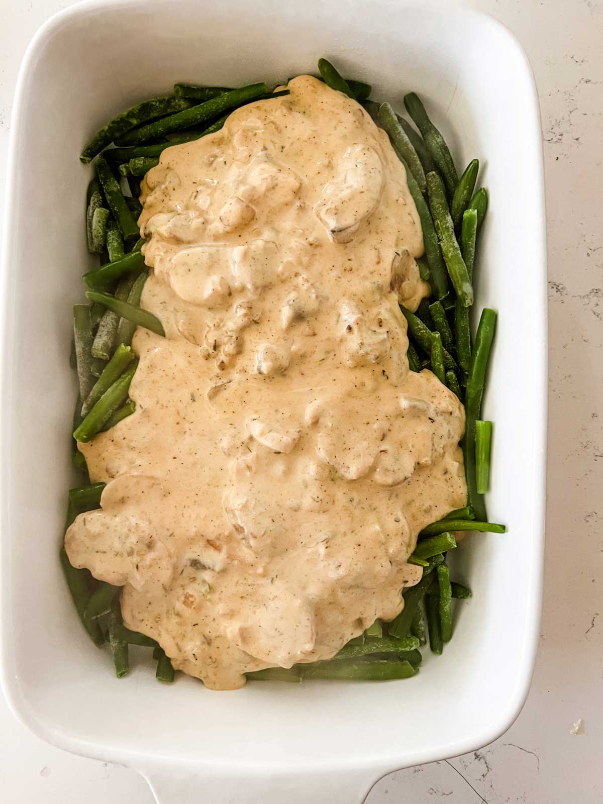 Frozen green beans with a homemade cream sauce on top of them in a casserole dish.
