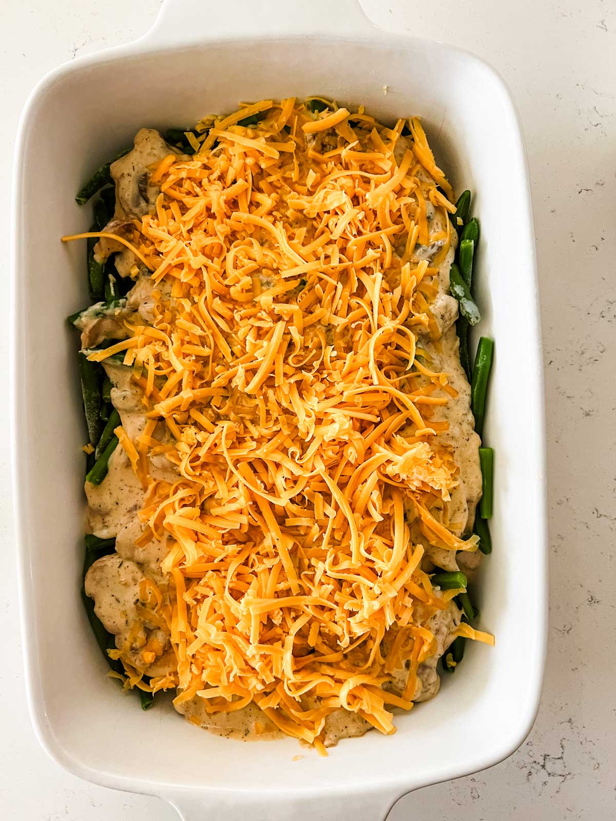 Green bean casserole with cheddar cheese on top of it ready for the oven.