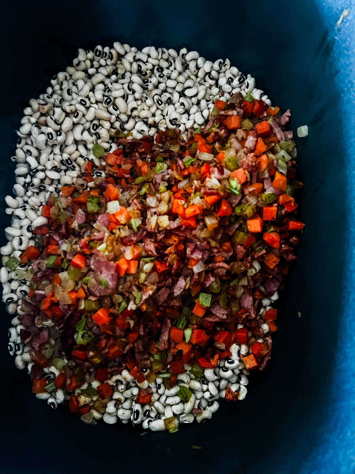 Dried black eyed peas in a slow cooker with onion, celery, carrot, garlic, and seasonings over them.