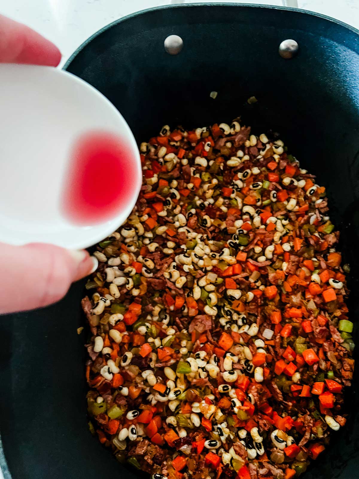 Vinegar being added to a slow cooker with black eyed peas and seasonings.