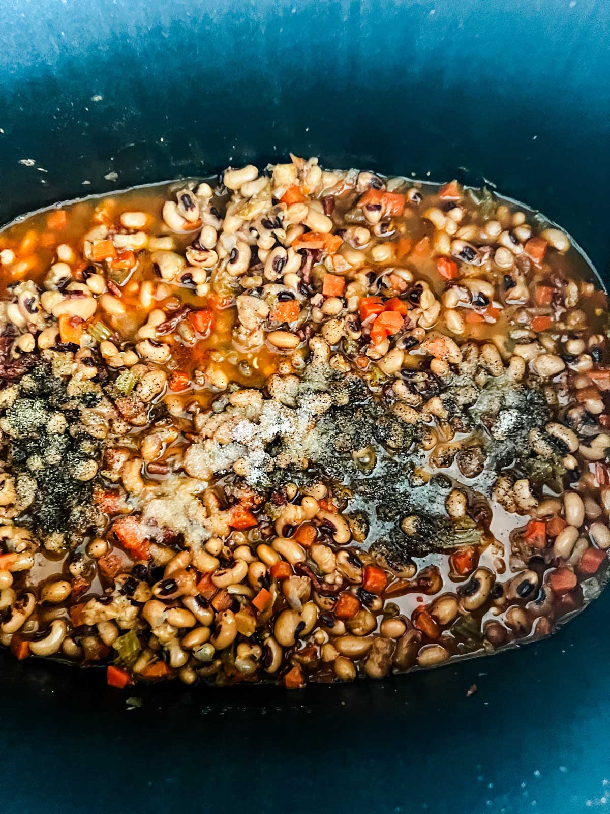 Overhead photo of salt and pepper being added to black eyed peas in a slow cooker.