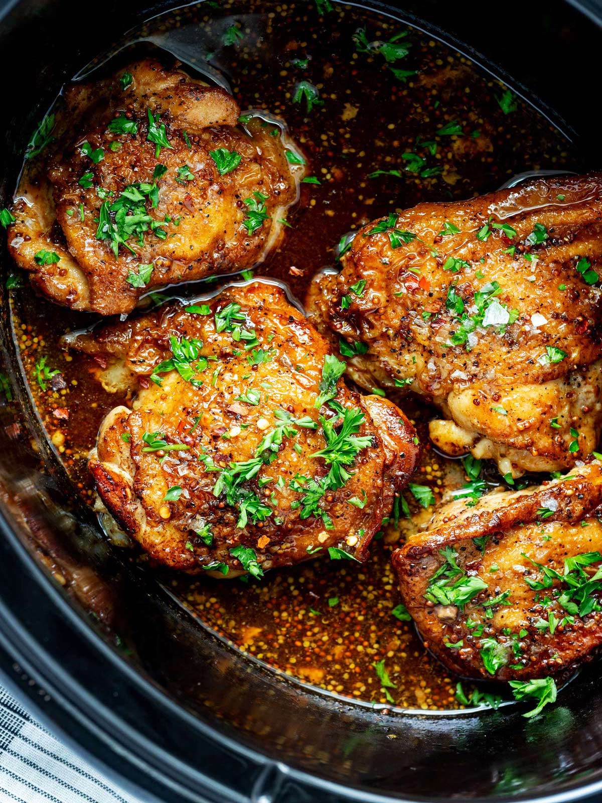 Close up photo of cooked chicken thighs in a slow cooker.