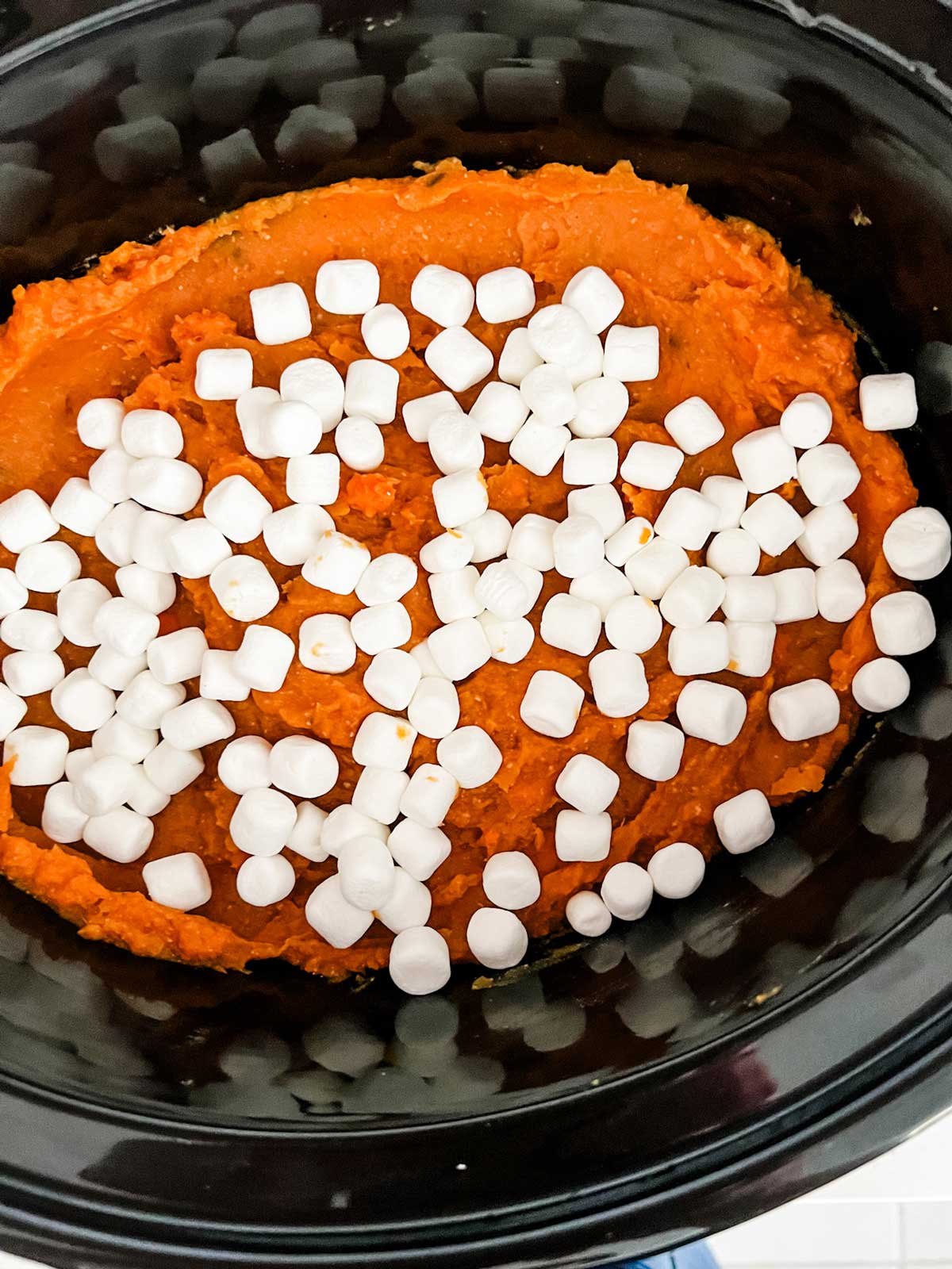 Crockpot sweet potato casserole with marshmallows on top of it in a slow cooker.
