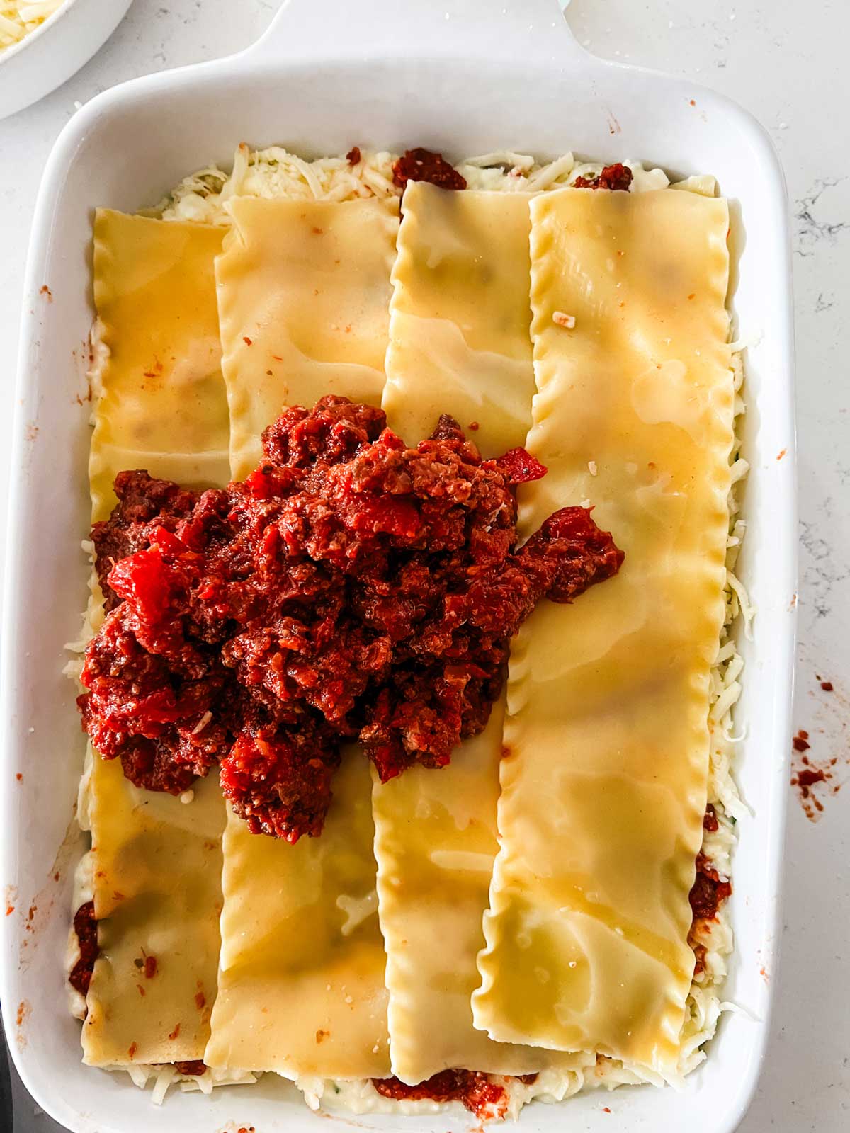Meat sauce being added on top of lasagna noodles as one of the final layers.