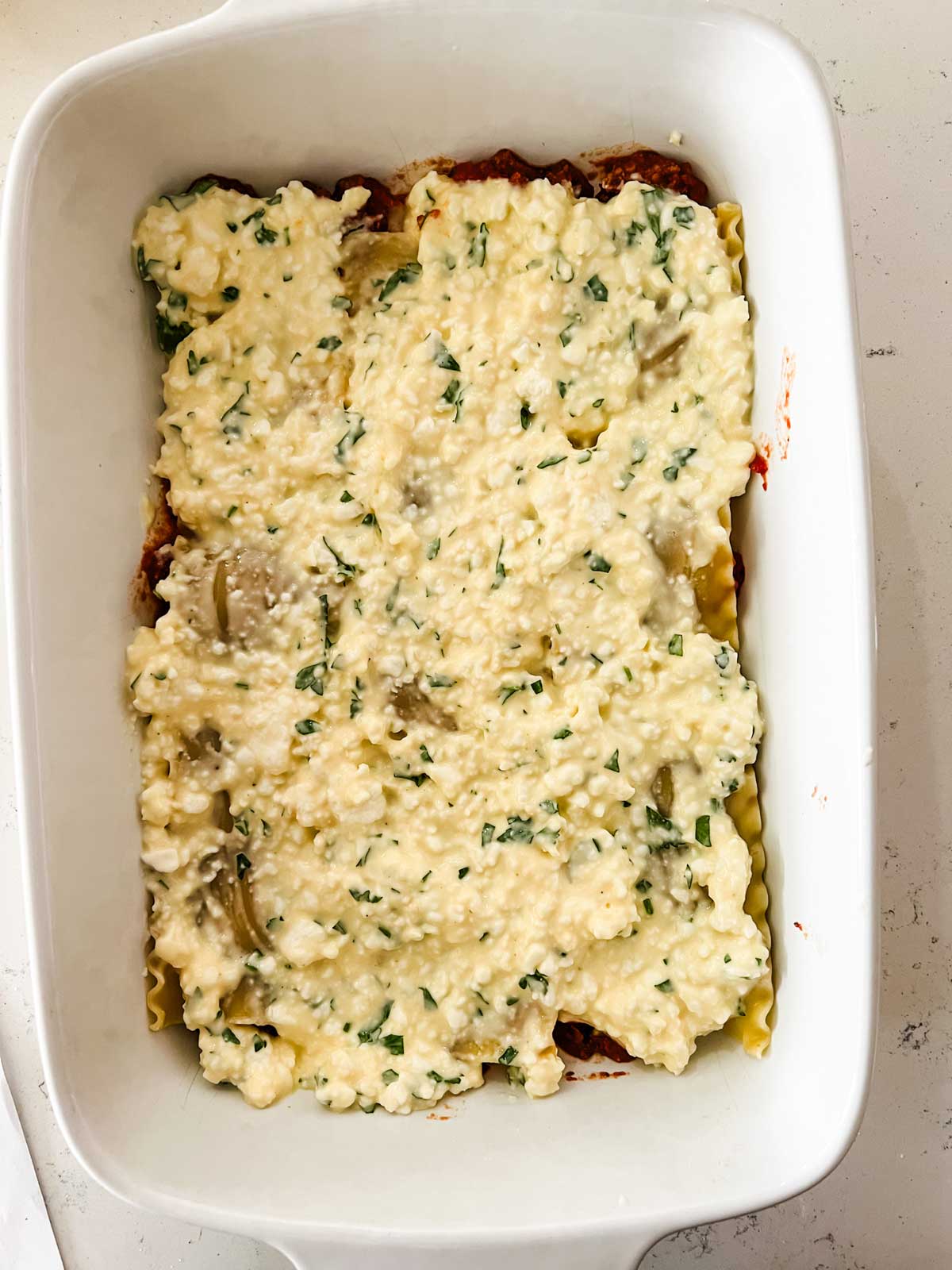 Cottage cheese over lasagna noodles in a casserole dish.