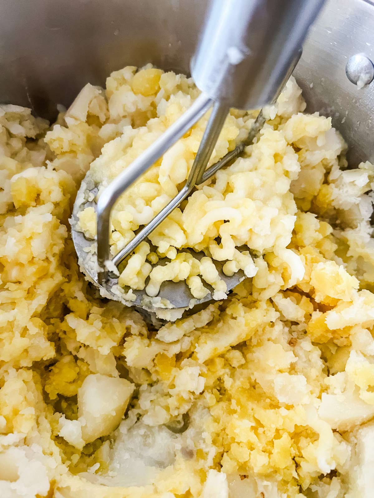 Potatoes being mashed with a potato masher.