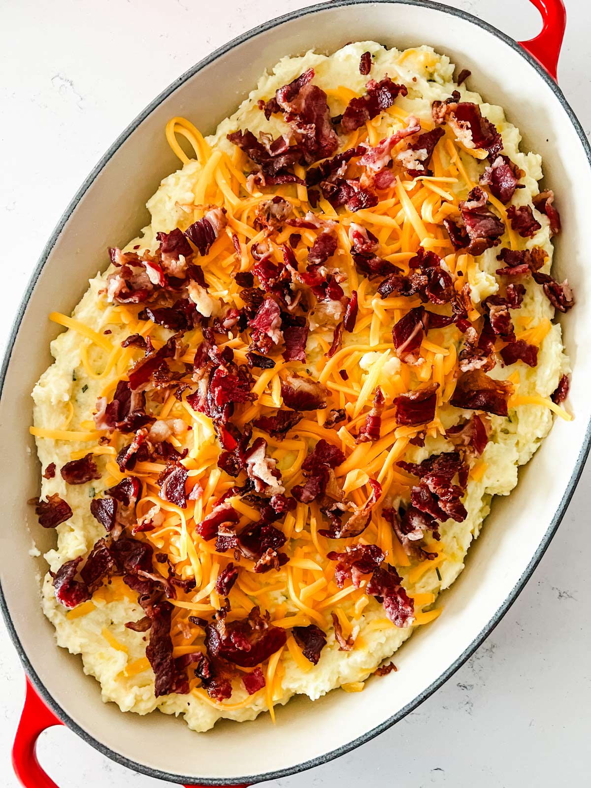 Mashed potatoes in a casserole dish with cheese and bacon on top.