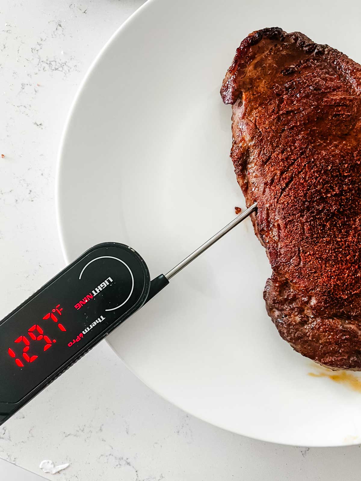 A steak that has been cooked in the Ninja Foodi to almost 130° F with a meat thermometer displaying the internal temperature.