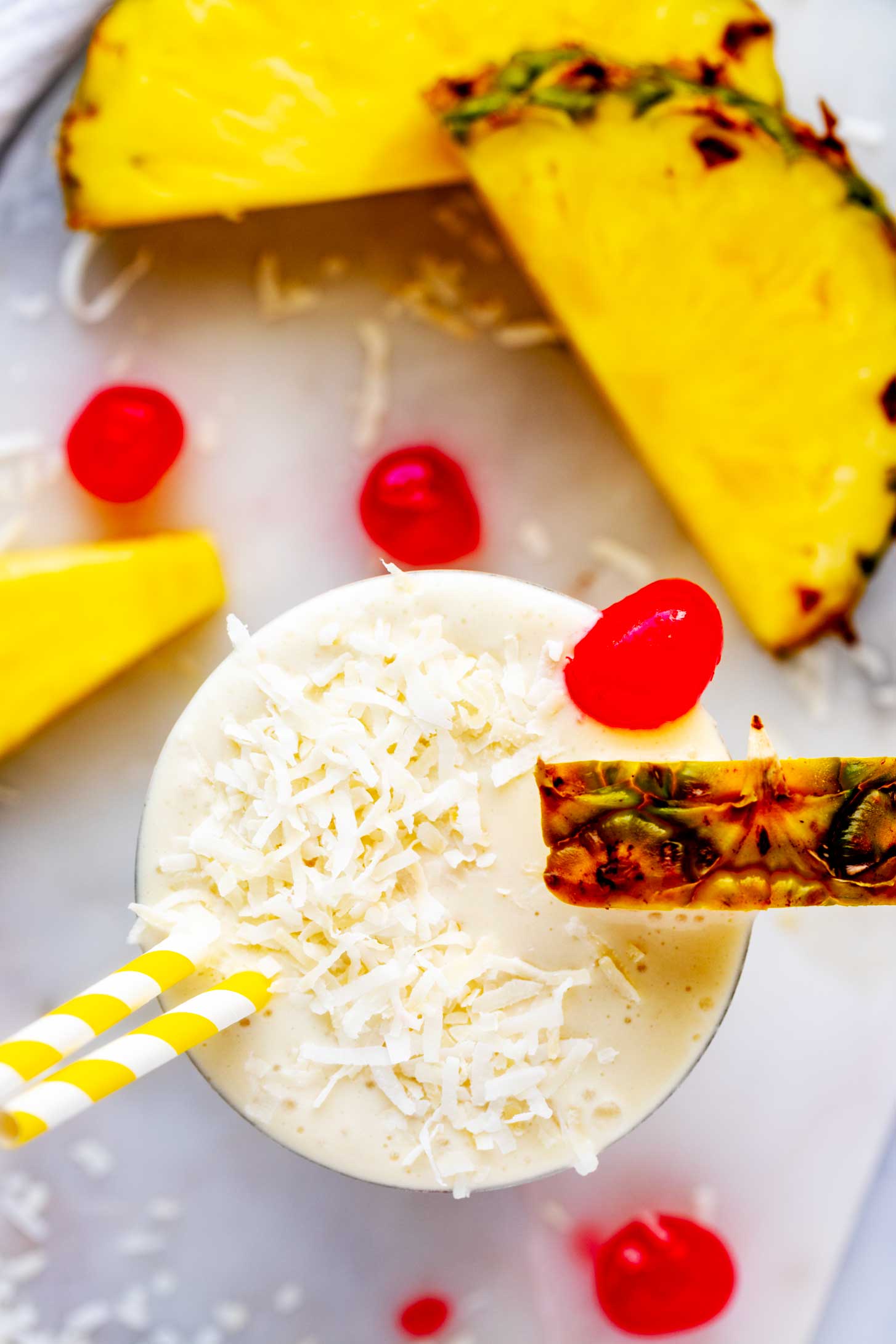 Overhead photo of a phina colada smoothie garnished with coconut, pineapple, and a cherry.