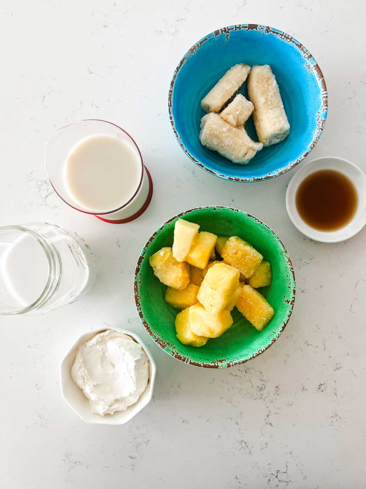 Overhead photo of pineapple, banana, oat milk, yogurt, and vanilla.