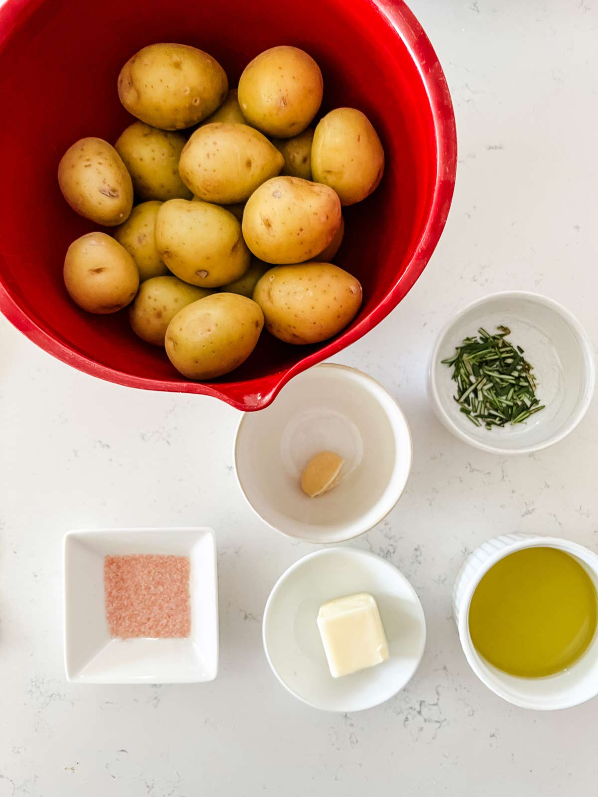 Overhead photo of yukon gold potatoes, rosemary, oil, butter, garlic, and salt.
