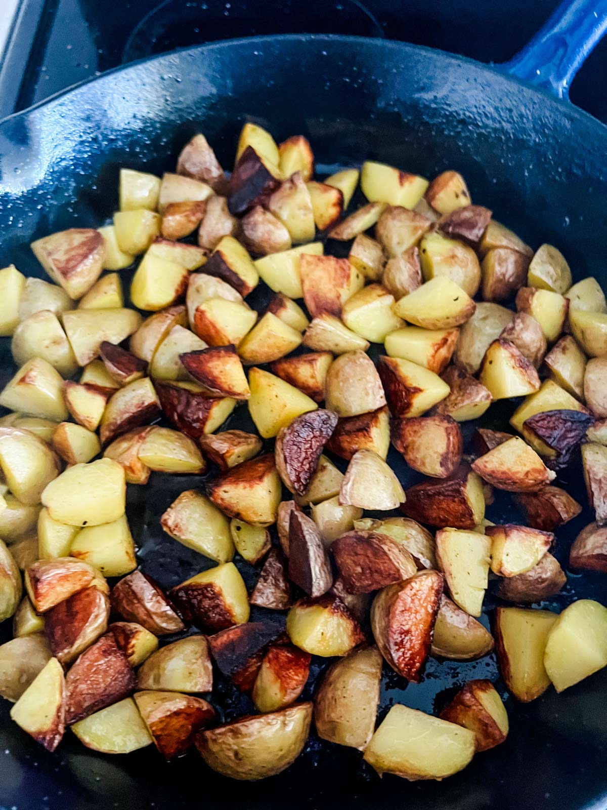 Skillet potatoes in a cast iron skillet that have started to get golden brown.
