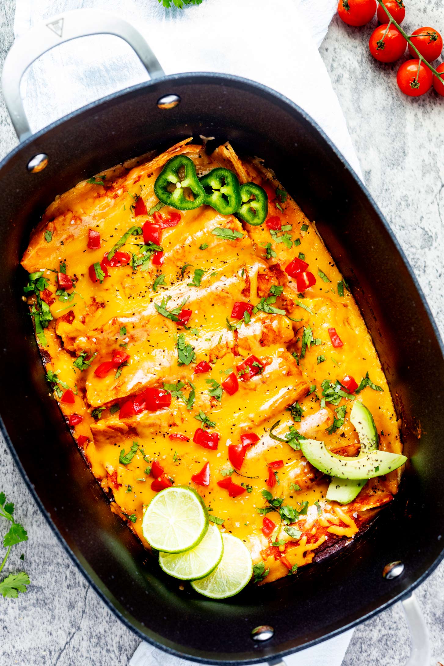 Slow cooker chicken enchiladas garnishes with tomato, jalapeno, lime and avocado in a Ninja Possible cooker.