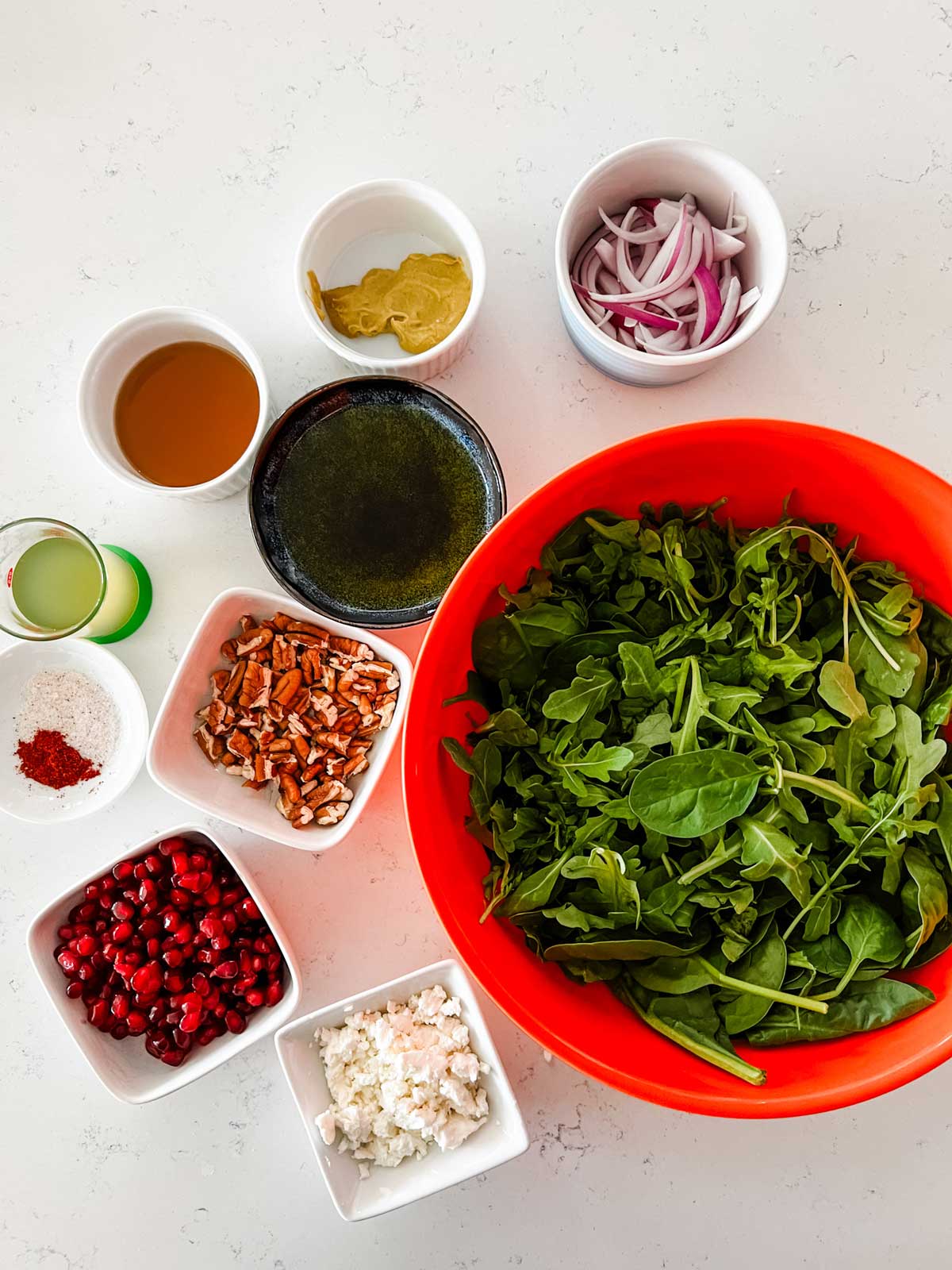 Overhead photo of spinach, arugula, red onion, goat cheese, pomegranat and dressing ingredients for a salad.