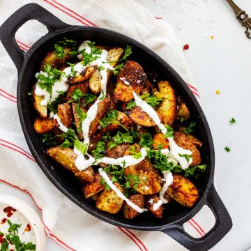 Overhead square photo of ranch potatoes in a cast iron dish drizzled with ranch dressing.