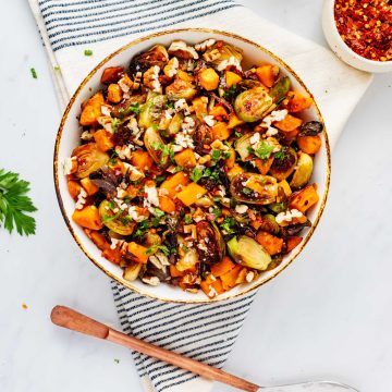 Square overhead photo of roasted Brussels sprouts and sweet potatoes in a rustic bowl garnished with parsley.