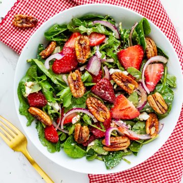 Square photo of a strawberry goat cheese salad in a shallow salad bowl sitting on a red and white napkin.