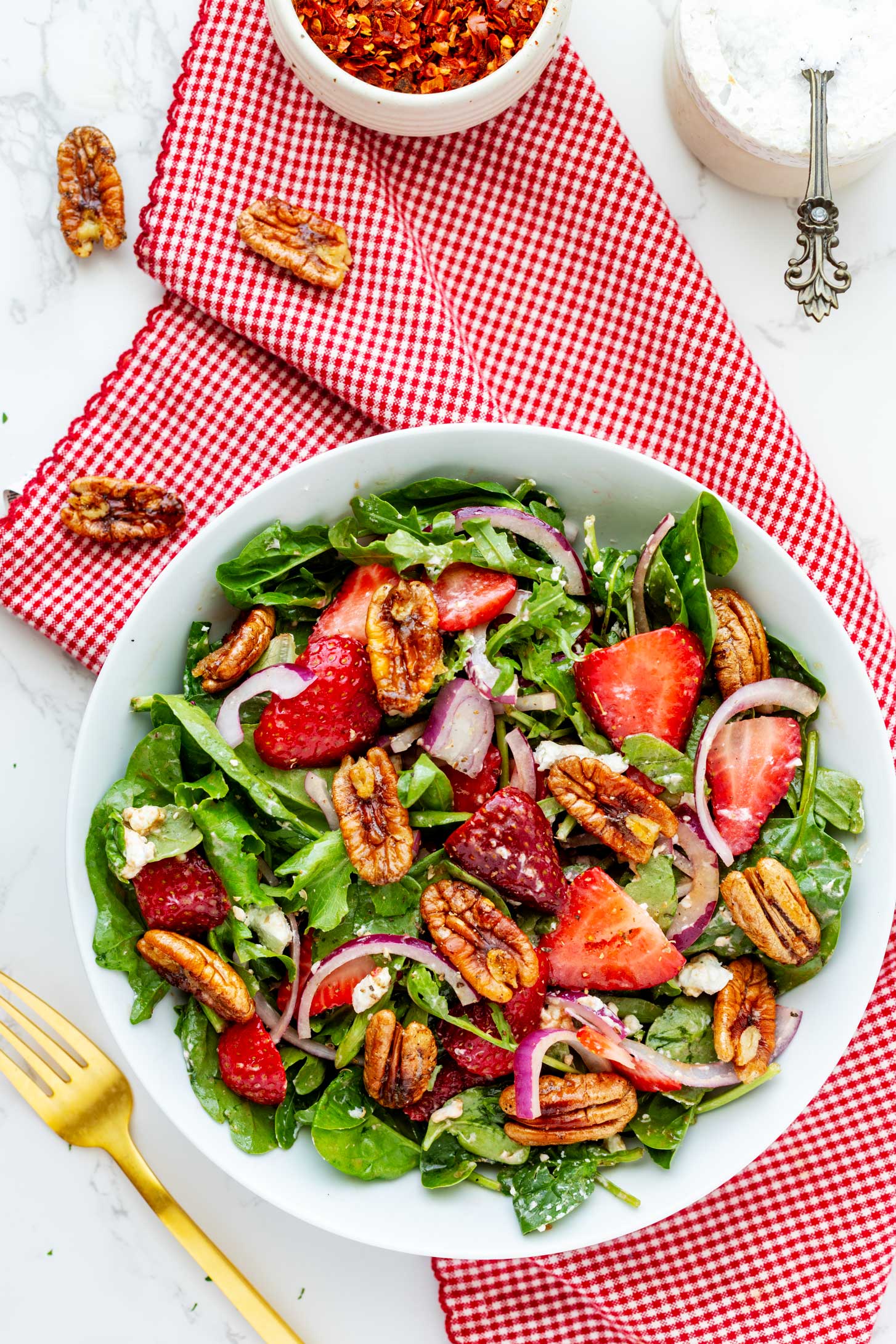 Overhead photo of a strawberry goat cheese salad in a shallow salad bowl sitting on a red and white napkin.