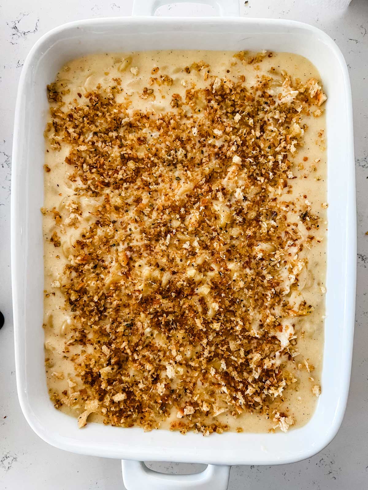 Breadcrumbs sprinkled on top of a white cheddar mach and cheese ready for the oven.