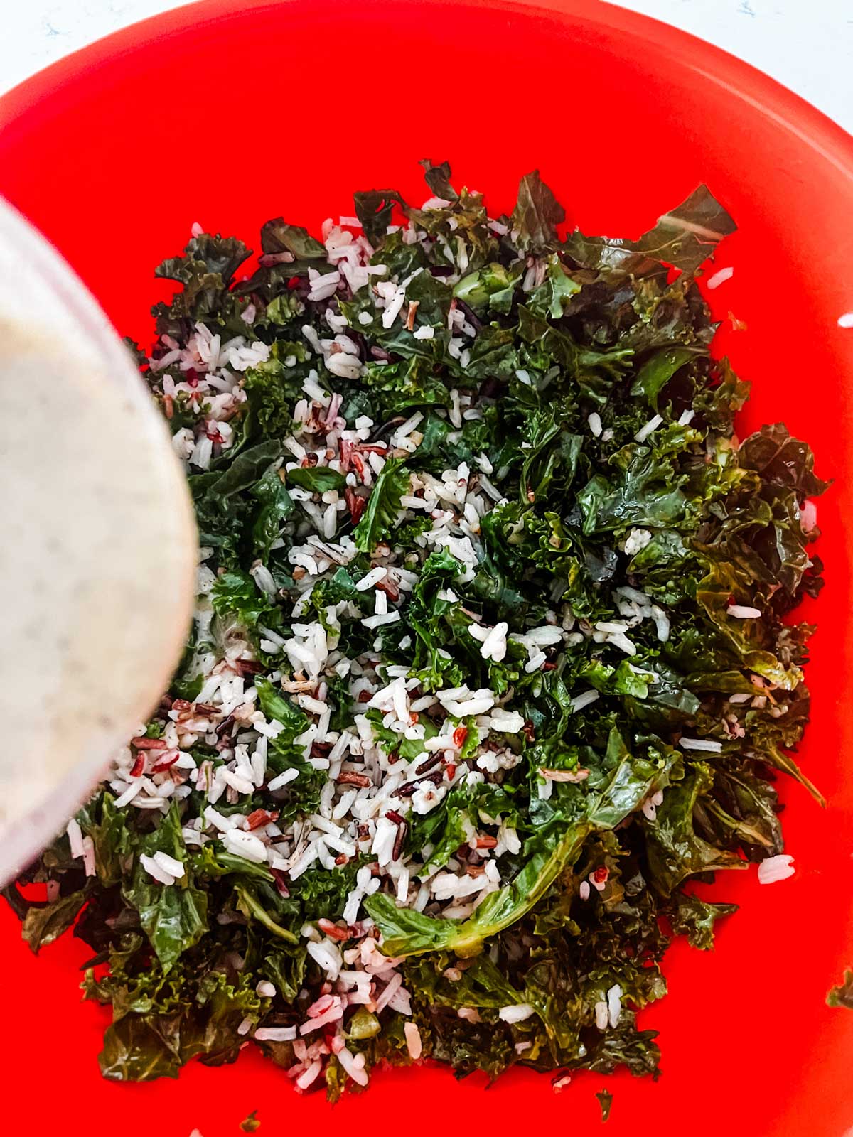 Dressing being poured over massaged kale and wild rice.