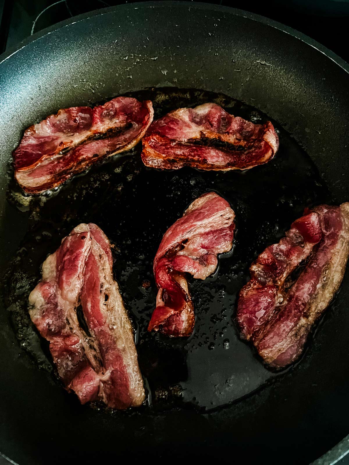 Photo of bacon cooking in a skillet.