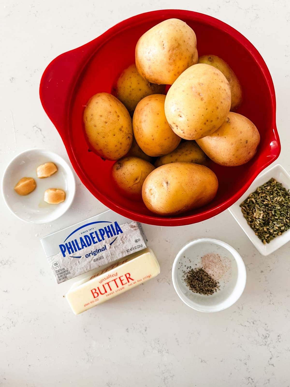 Overhead photo of a bowl of yukon gold potatoes, garlic, cream cheese, butter, and seasonings.
