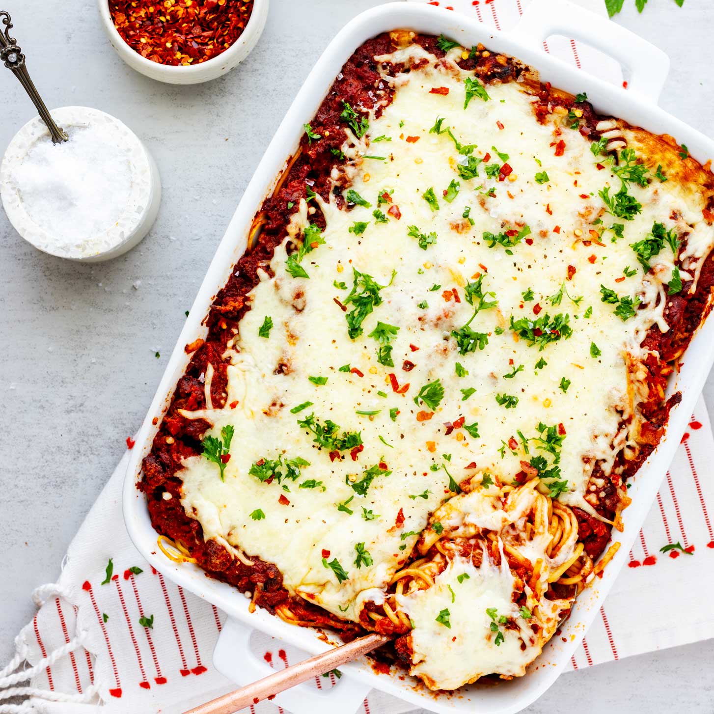 Overhead photo of a casserole dish with baked spaghetti with cream cheese and a serving spoon coming from it.