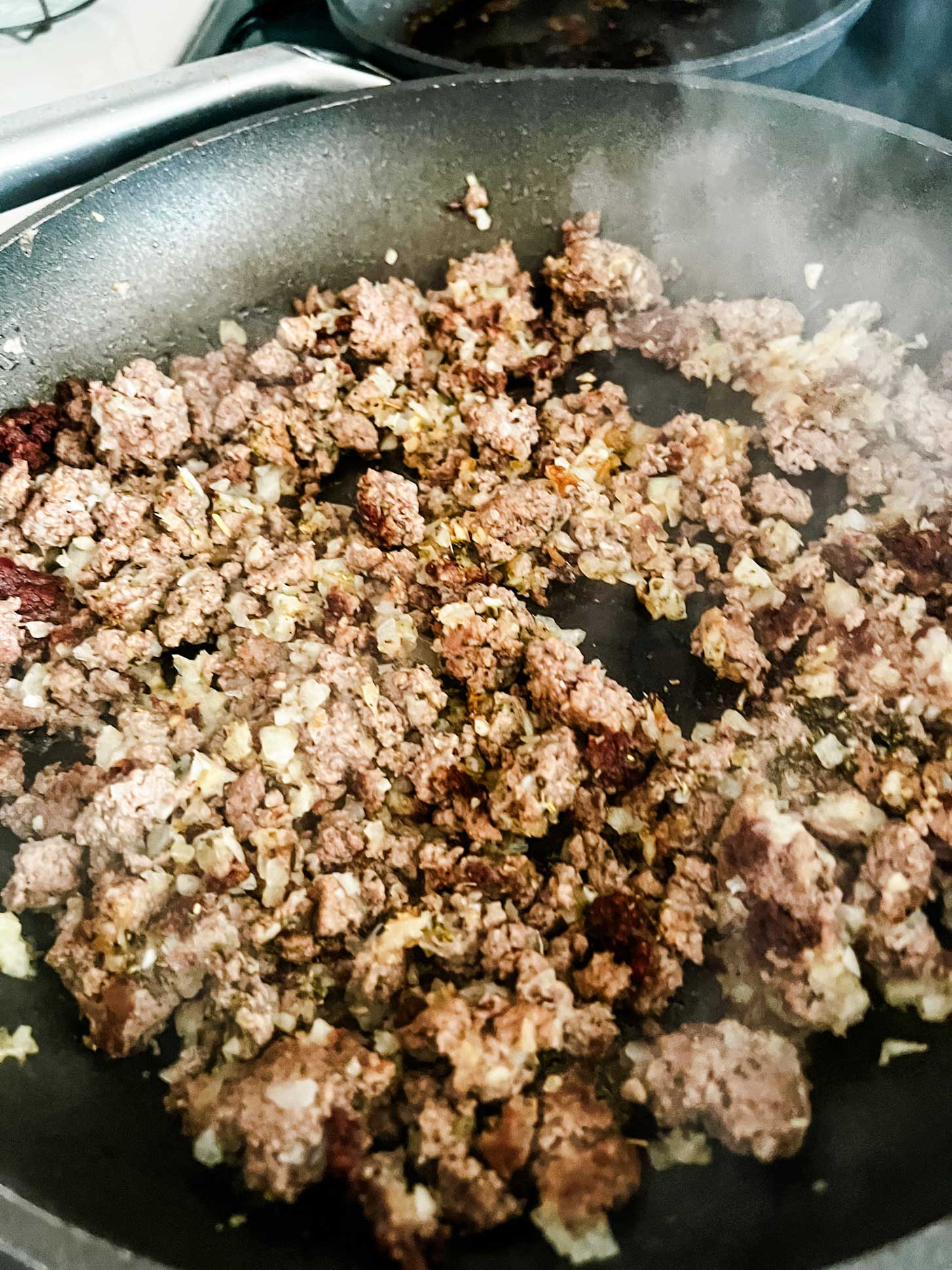 Onion, ground beef, and seasonings in a skillet.
