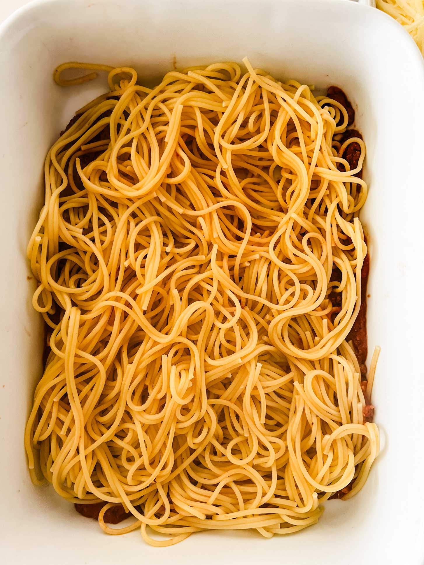 Spaghetti noodles on top of marinara in a casserole dish.
