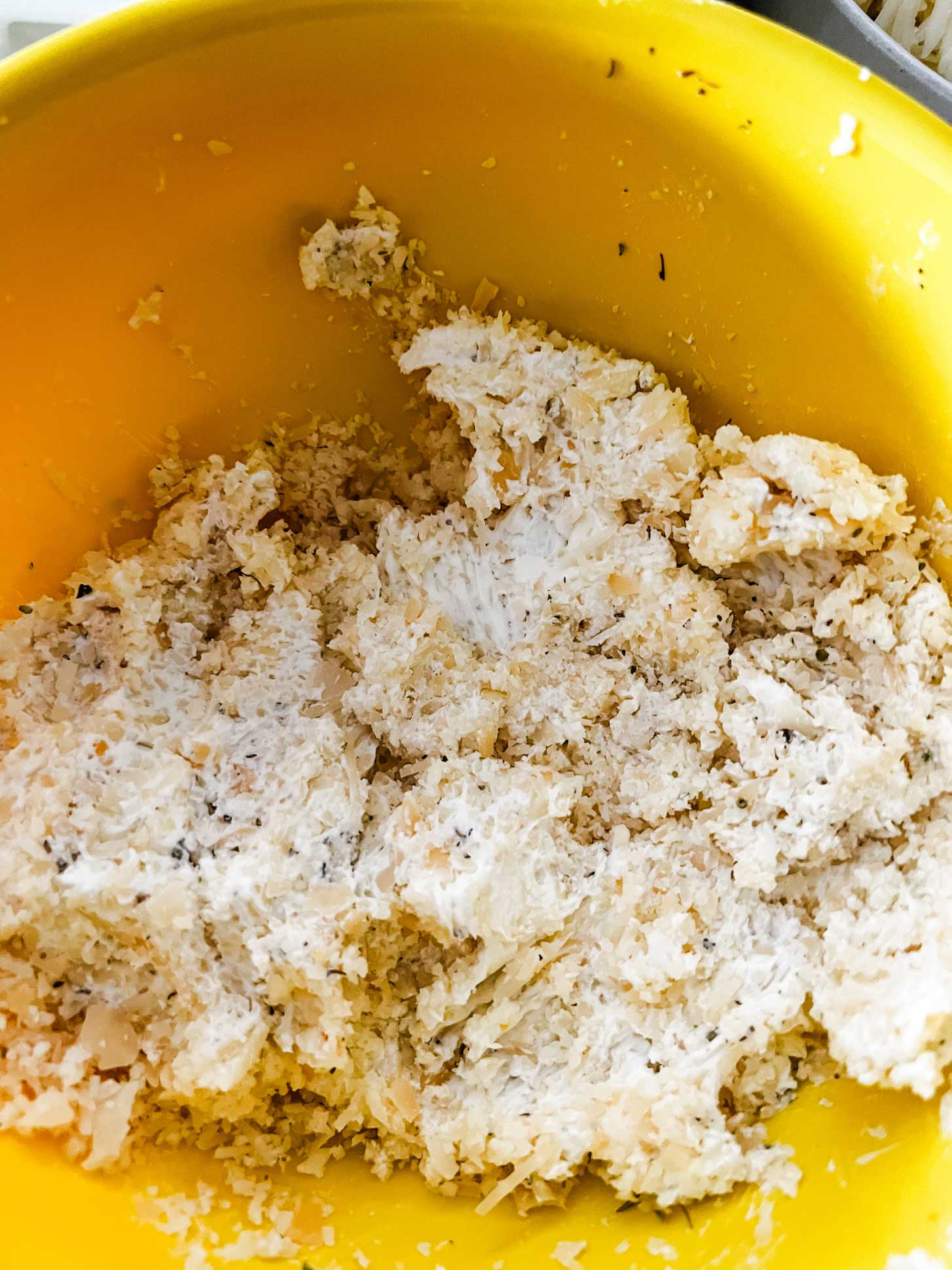 A mixture of cream cheese, parmesan cheese, and seasonings in a yellow bowl.