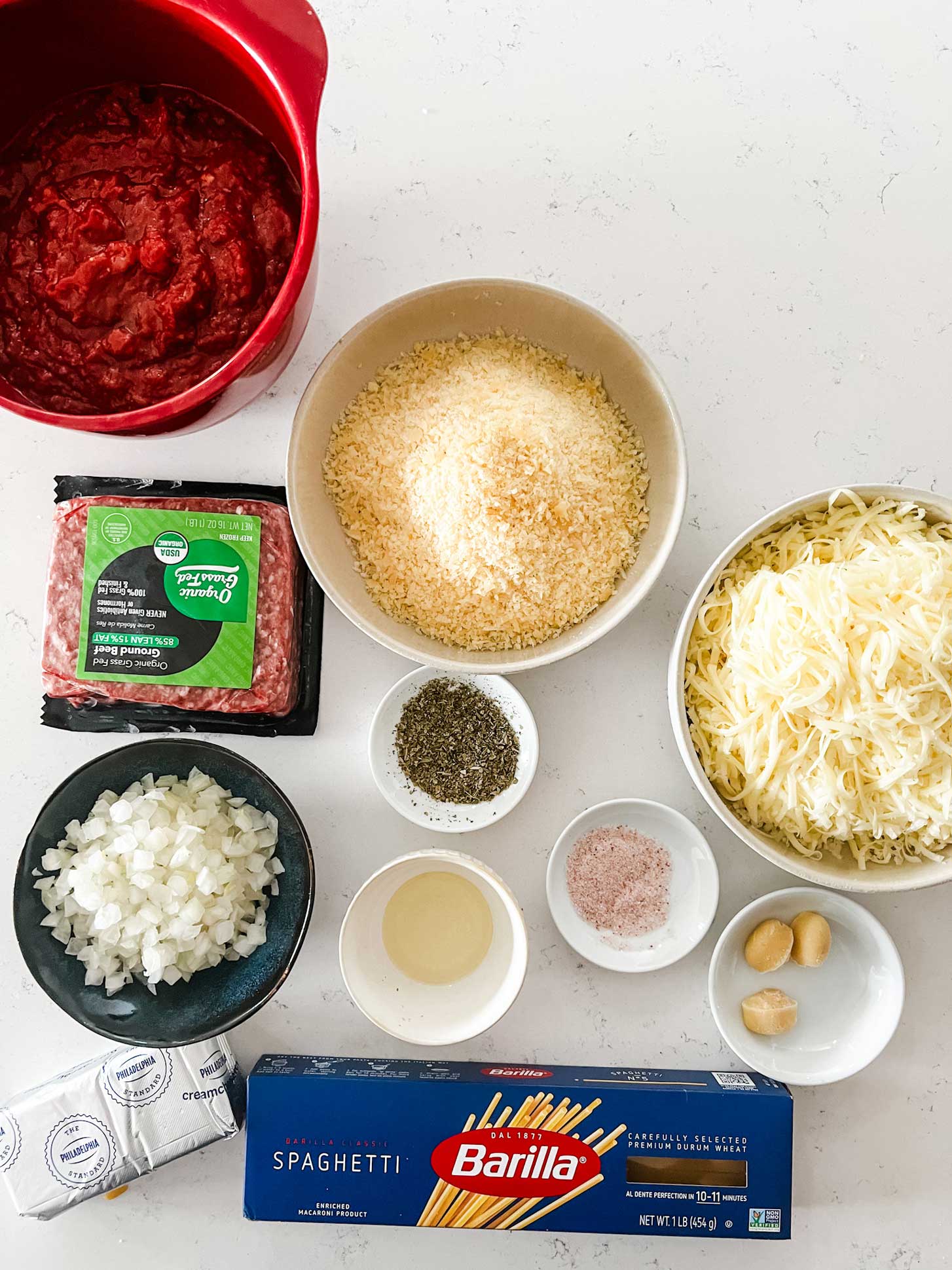 Overhead photo of marinara, ground beef, onion, parmesan, mozzarella, cream cheese, spaghetti, garlic, oil, and seasonings.
