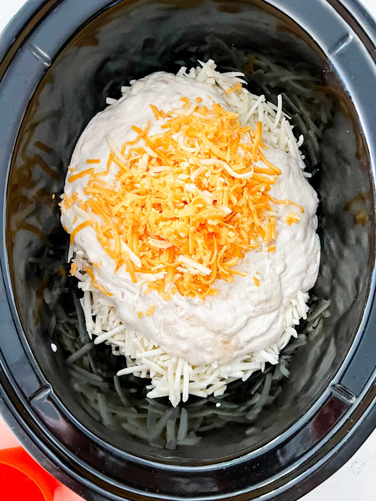 Photo of cheese and a homemade creamy sauce being added to hash browns in a crockpot.