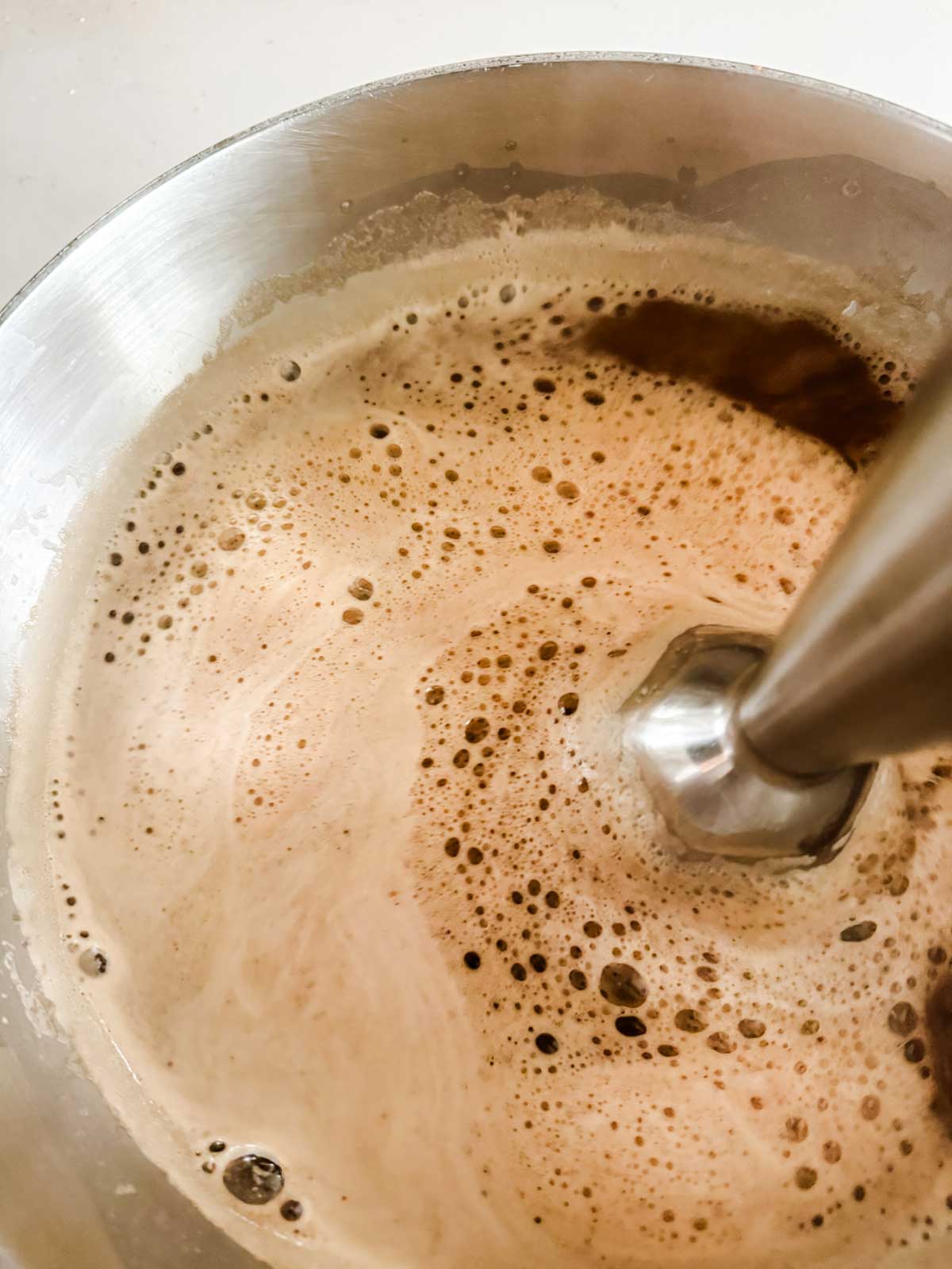 An immersion blender frothing a dirty chai latte.