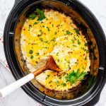 Overhead square photo of a crockpot hash brown casserole in a slow cooker with a spoon.