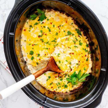 Overhead square photo of a crockpot hash brown casserole in a slow cooker with a spoon.