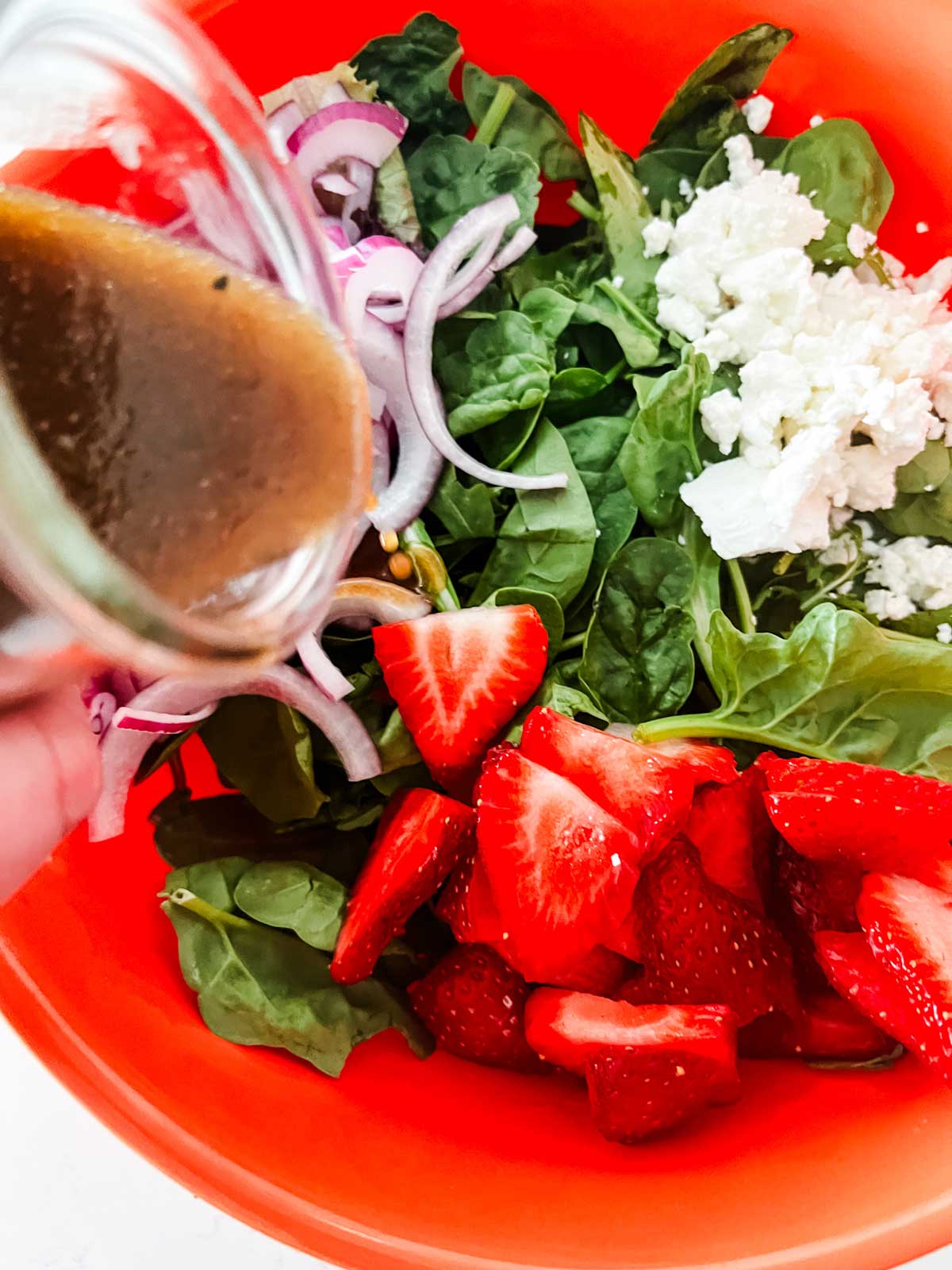 Photo of balsamic vinegar dressing being poured onto a strawberry goat cheese salad.