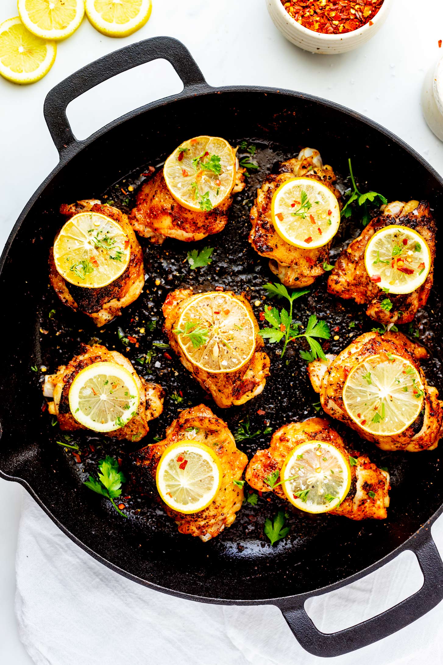 Close up overhead photo of cast iron chicken thighs garnished with lemon and parsley.