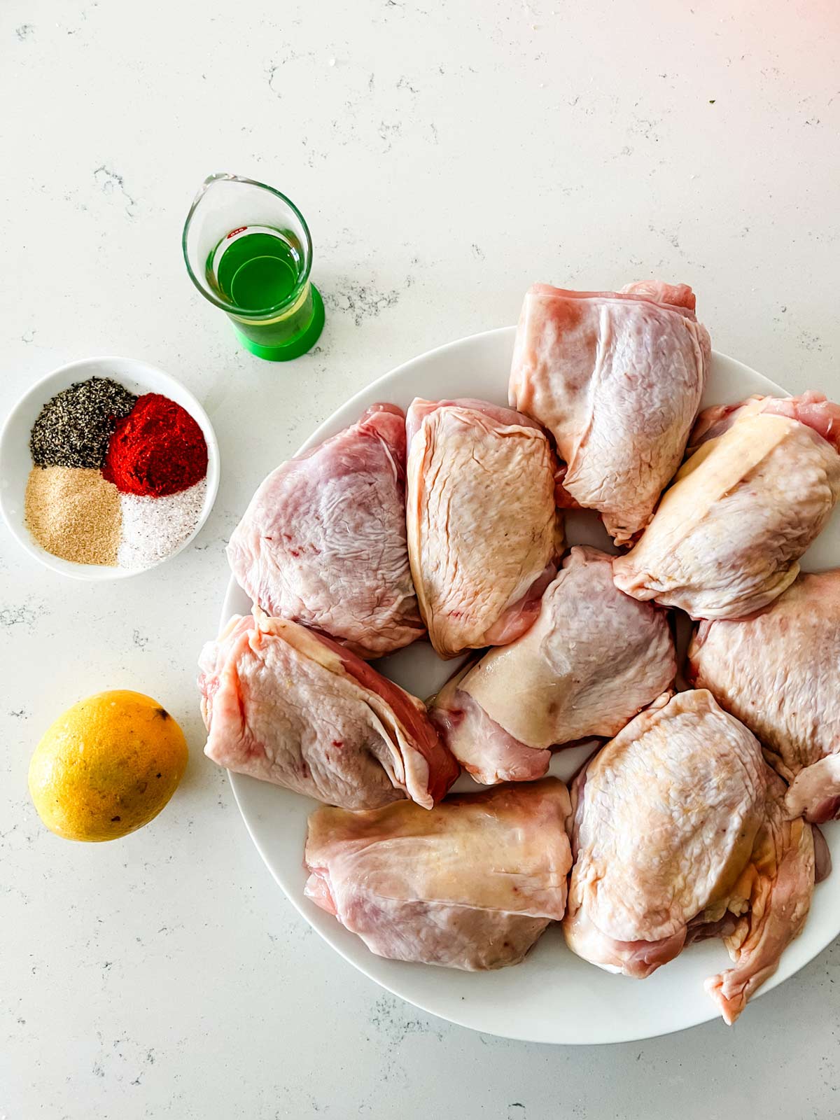 Overhead photo of chicken thighs, lemon, oil, and seasonings.