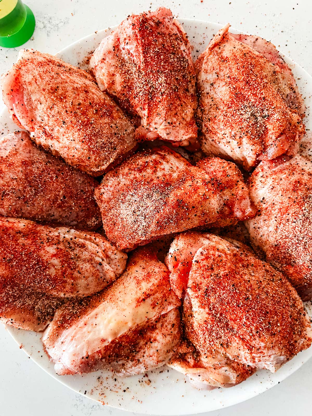 Close up photo of seasoned chicken thighs on a white plate.