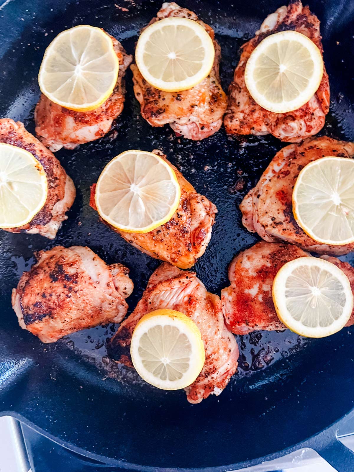 Chicken thighs with lemon on top in a cast iron skillet.