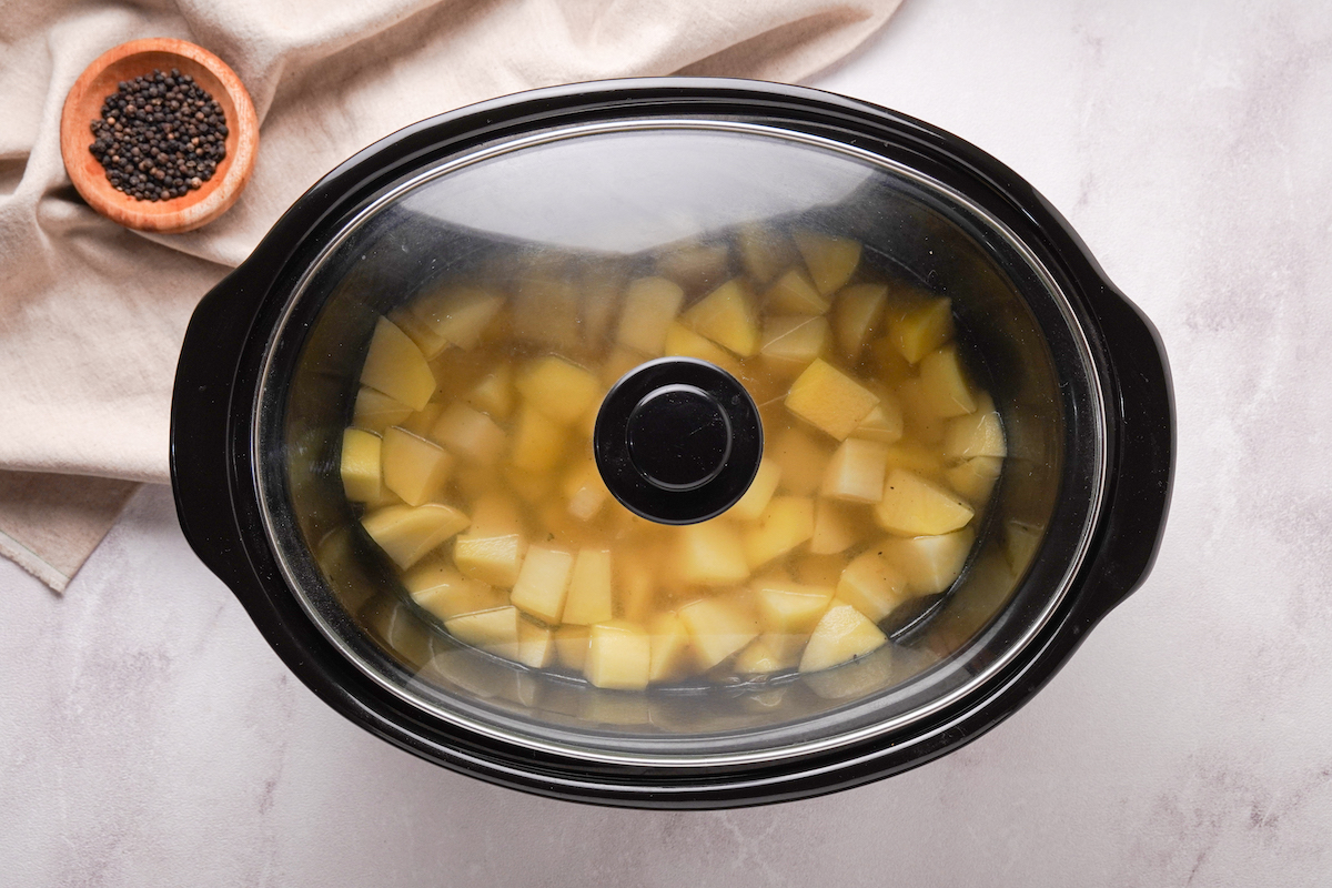 A slow cooker with the lid on it with ingredients for potato soup cooking.