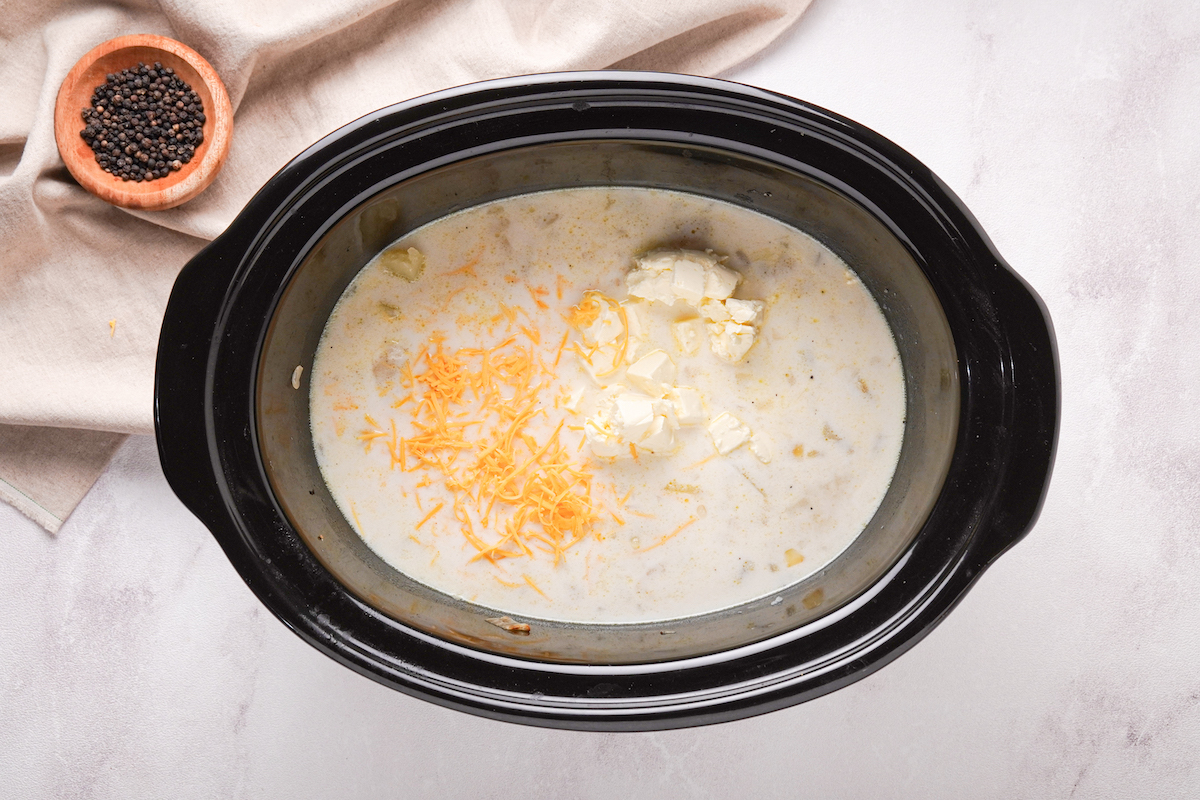 Cream cheese, cream, and cheese added to a slow cooker to make potato soup.