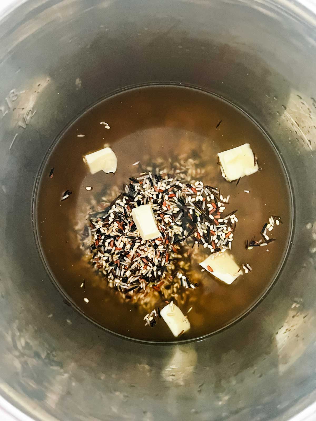 Overhead photo of broth, wild rice, and butter in and Instant Pot.